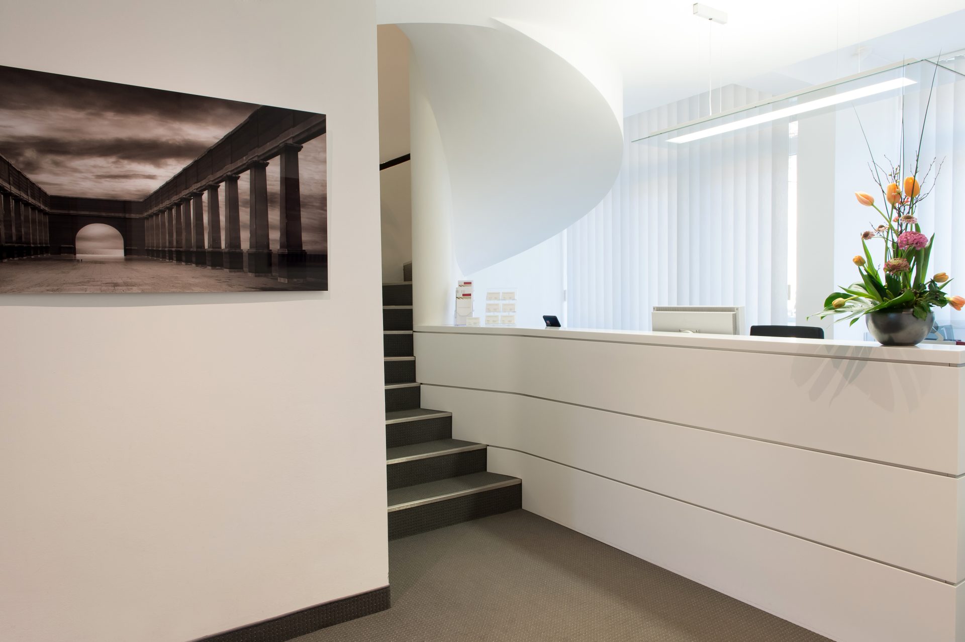 Moderner Empfangsbereich mit Rezeption und Treppe.